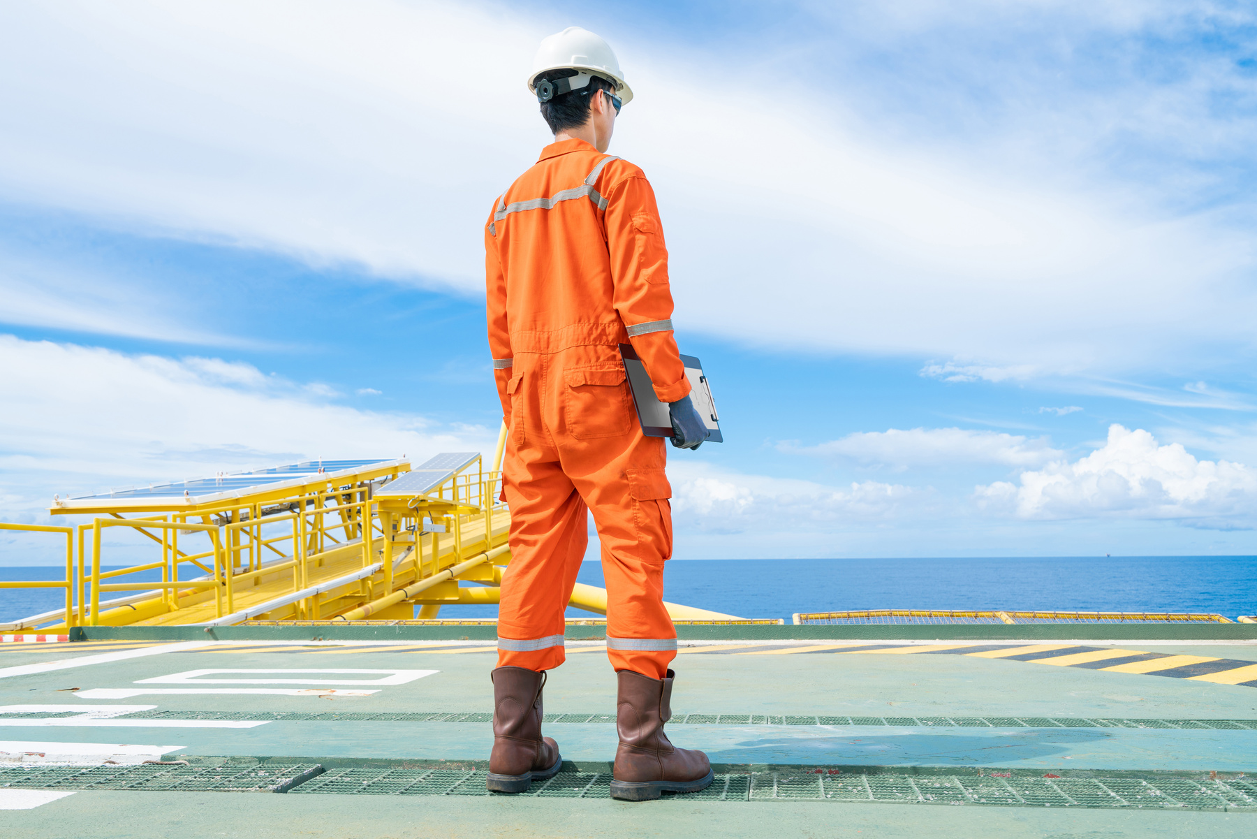 An offshore oil rig worker wearing personal protective equipment and standing on offshore wellhead remote platform.